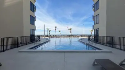 a swimming pool between two buildings with palm trees at Sunbird Resort - 11th Floor - Free Beach Chairs - by Sunbird Rentals in Panama City Beach
