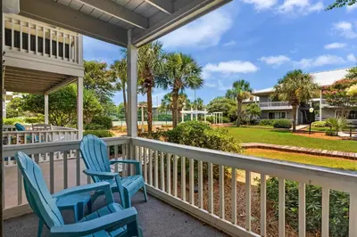 a porch with two blue chairs and palm trees at Sunny Daze at Beachwood Villas - Walk to Beach Outdoor Pools & More in Santa Rosa Beach