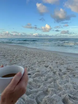 a person holding a cup of coffee on the beach at Beach Across Street, Walk to Restaurants, 2 Pools, Beach Gear in Panama City Beach