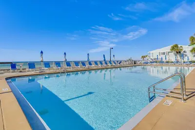 a swimming pool with chairs and the ocean in the background at Beach and Pool Access Regency Towers Condo in PCB! in Panama City Beach