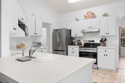 a kitchen with white cabinets and a stainless steel refrigerator at Pet Friendly Beach House - Baby Blue Heron by Panhandle Getaways in Panama City Beach