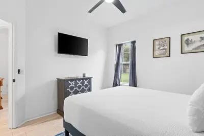 a white bedroom with a bed and a flat screen tv at Pet Friendly Beach House - Baby Blue Heron by Panhandle Getaways in Panama City Beach