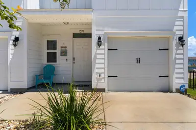 a white house with two garage doors and a blue chair at Shell We Stay (3/2.5) in Panama City Beach
