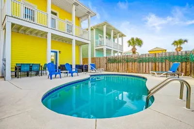 a swimming pool with blue chairs and a yellow house at PCB Private Pool Home, Sleeps 14, Dog Friendly, Near Beach in Panama City Beach