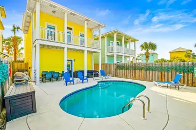 a pool in front of a yellow house with blue chairs at PCB Private Pool Home, Sleeps 14, Dog Friendly, Near Beach in Panama City Beach