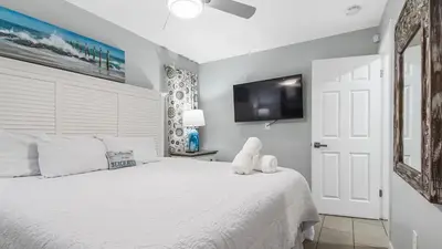 a bedroom with a white bed and a flat screen tv at Renovated Condo 4-Min Walk to Beach & Pools in Panama City Beach