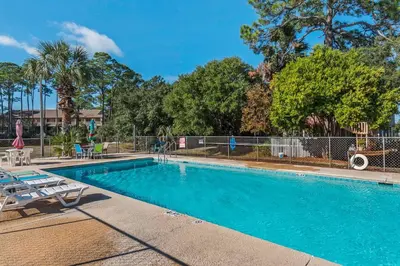 a swimming pool with two lounge chairs and trees at Pirates Cove Inlet Unit H (0/1) in Panama City Beach