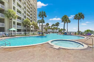 a swimming pool with palm trees and a building at Grand Panama Beach Resort by Panhandle Getaways in Panama City Beach