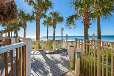 a wooden walkway to the beach with palm trees at Calypso 1-1805 by Emerald Coast Retreats in Panama City Beach