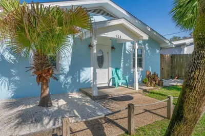 a blue house with a palm tree in front of it at Latitude Adjustment - Private Pool, Game Room, Spacious Home, Pets OK, 5 Min Walk to Beach! in Panama City Beach