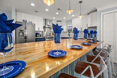 a kitchen with a long wooden table with blue wine glasses at Latitude Adjustment - Private Pool, Game Room, Spacious Home, Pets OK, 5 Min Walk to Beach! in Panama City Beach