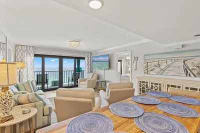 a living room with a table and a dining room with a view at Commodore 1106 in Panama City Beach