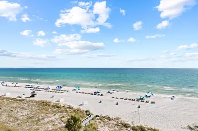 a beach with chairs and umbrellas and the ocean at Commodore 0608 in Panama City Beach