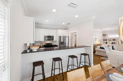 a kitchen and living room with white cabinets and stools at Fore Seasons by 30A Escapes in Seagrove Beach