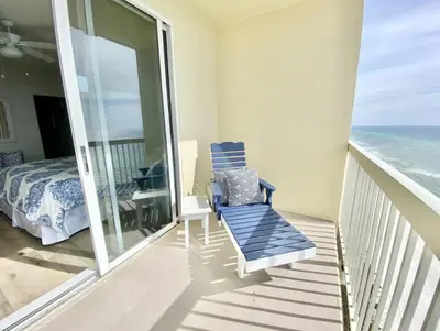 a balcony with a blue chair and a bed and the ocean at Celadon 2005 by Emerald Coast Retreats in Panama City Beach