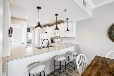 a kitchen with white cabinets and a table with stools at HP 35W Gulf Front Condo by 30A Escapes in Rosemary Beach