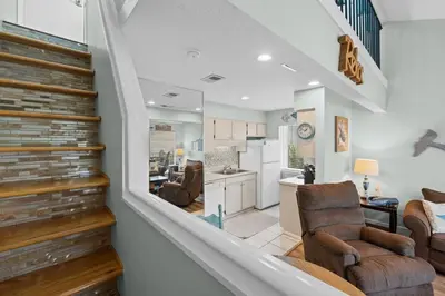 a living room with a staircase and a kitchen at Quiet East End PCB Condo w/ Direct Beach Access & Balcony in Panama City Beach
