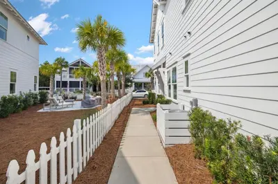 a white fence next to a house with palm trees at Coastal Grace in Inlet Beach