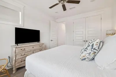 a white bedroom with a bed and a flat screen tv at Our Oasis in Inlet Beach