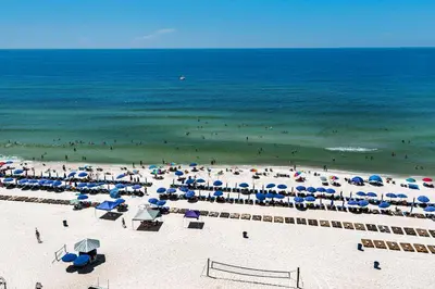 a beach with many umbrellas and people in the ocean at Calypso 1-202 by Emerald Coast Retreats in Panama City Beach
