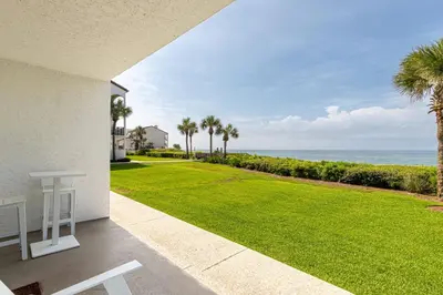 a patio with a lawn with palm trees and the ocean at Psalms in Santa Rosa Beach