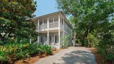 a white house with a porch and trees at Magnolia Breeze in Santa Rosa Beach