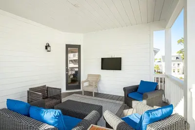 a screened porch with chairs and a tv on a white wall at Salty Sons in Inlet Beach