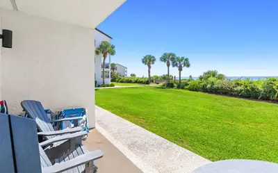 a porch with chairs and a lawn with palm trees at The Palms in Santa Rosa Beach