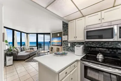 a kitchen with a stove top oven next to a living room at Sunbird low Floor 2BR! Free Beach Chair Service! by Dolce Vita Getaways PCB in Panama City Beach