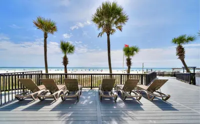 a boardwalk with chairs and palm trees and the beach at Renovated Penthouse! Free Beach Chairs Included! by Dolce Vita Getaways PCB in Panama City Beach