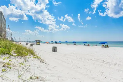 a beach with people sitting under umbrellas and the ocean at 3B - The Seaglass Shack in Panama City Beach