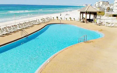 a swimming pool next to a beach with chairs and the ocean at Treasure Island 1102 in Panama City Beach