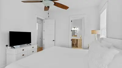 a white bedroom with a ceiling fan and a television at Serene 30A Getaway Steps from the Gulf with BBQ Wraparound Porch 30A Fade Away by AvantStay in Santa Rosa Beach