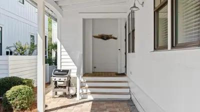 a white house with a front porch with a stroller at Serene 30A Getaway Steps from the Gulf with BBQ Wraparound Porch 30A Fade Away by AvantStay in Santa Rosa Beach