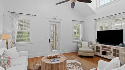 a living room with white walls and a flat screen tv at Serene 30A Getaway Steps from the Gulf with BBQ Wraparound Porch 30A Fade Away by AvantStay in Santa Rosa Beach
