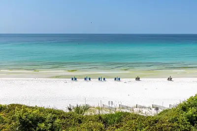 a beach with blue chairs and the ocean at 4 BR GULF Front Condo, Bikes, & Community Pool in Seagrove Beach