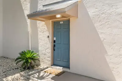 a blue door on a white building with a plant at Turtle Cove at Sugar Beach #E16 by Nautical Properties Vacation Rentals in Panama City Beach