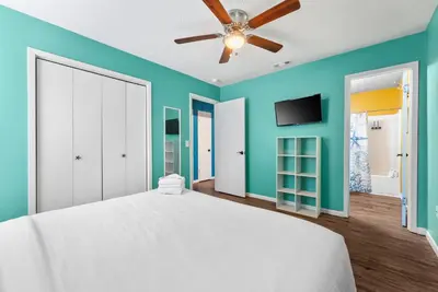 a bedroom with a white bed and a ceiling fan at Sunset Ave Beach House - Golf Cart, Pool, Hot Tub in Panama City Beach