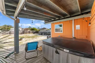 a covered deck with a table and a blue chair at Sunset Ave Beach House - Golf Cart, Pool, Hot Tub in Panama City Beach