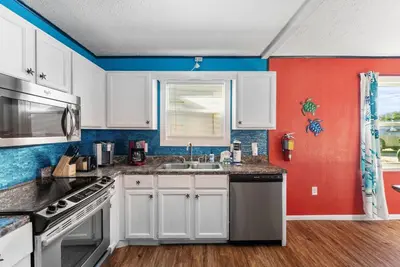 a kitchen with white cabinets and a red wall at Sunset Ave Beach House - Golf Cart, Pool, Hot Tub in Panama City Beach