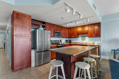 a kitchen with a stainless steel refrigerator and bar with stools at Beach Resort Condo with 5 Pools! Steps to Beach! by Dolce Vita Getaways PCB in Panama City Beach