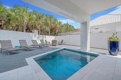 a swimming pool on a patio with chairs and a fence at Sea Turtle Retreat in Seagrove Beach