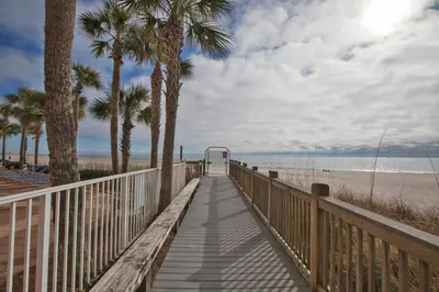 a wooden walkway to the beach with palm trees at Sterling Reef Beach Resort in Panama City Beach