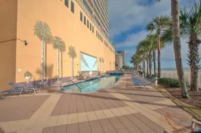 a swimming pool with palm trees next to a building at Sterling Reef Beach Resort in Panama City Beach