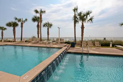 a large swimming pool with palm trees and chairs at Sterling Reef Beach Resort in Panama City Beach