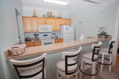 a kitchen with a counter with chairs and a refrigerator at Ocean Ritz 1501 in Panama City Beach