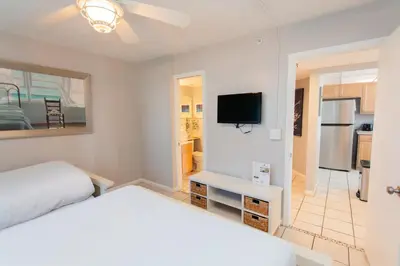 a white bedroom with a bed and a tv at Summerhouse 1005a in Panama City Beach