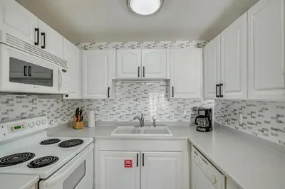 a white kitchen with white cabinets and a sink at Walk to Pools and Outdoor Bar! Oceanfront PCB Gem in Panama City Beach