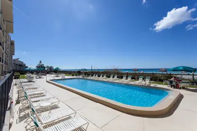 a swimming pool with chairs and the ocean in the background at Mariner West 508 in Panama City Beach