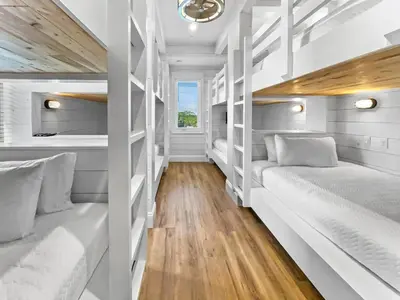 two beds in a room with wooden floors and white walls at Summer Wind l Ocean Views, Steps to Beach, Private Pool and Jacuzzi, Golf Cart, Bikes, Ample Parking in Seagrove Beach
